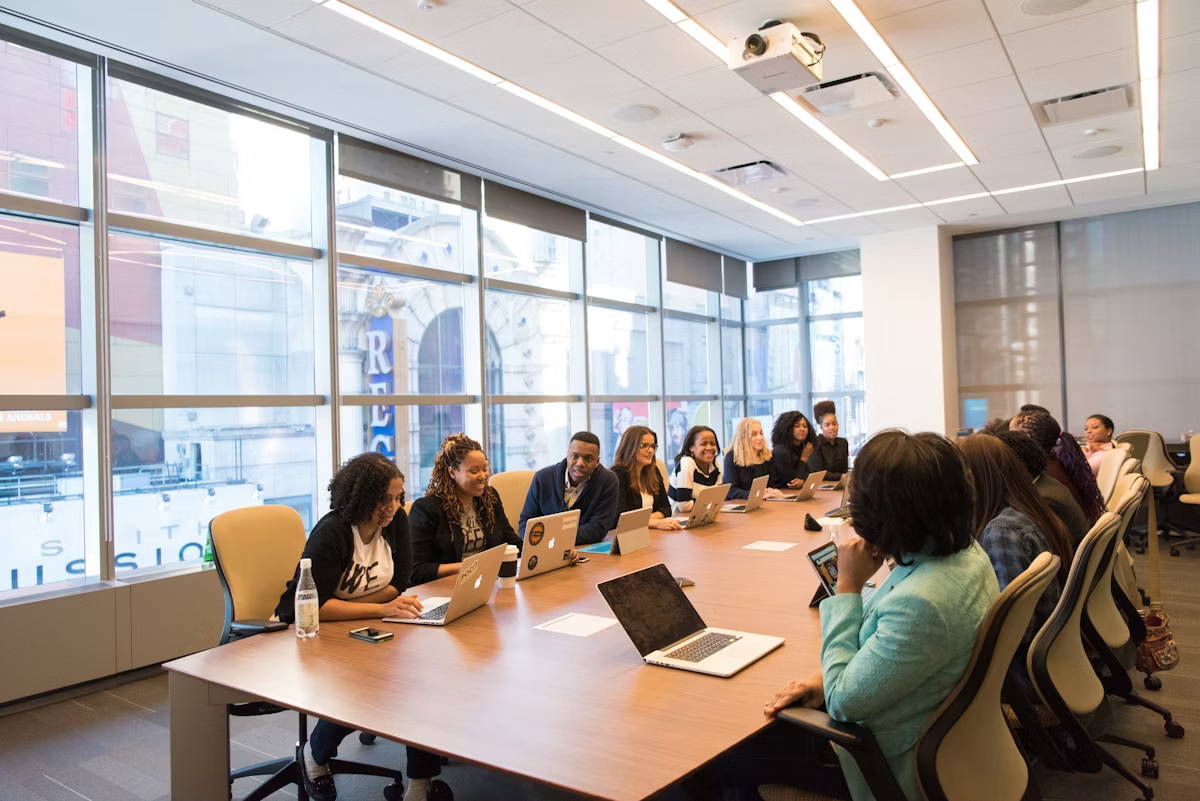 A group of colleagues sitting beside a long wooden table with laptops open, reviewing a plan together
