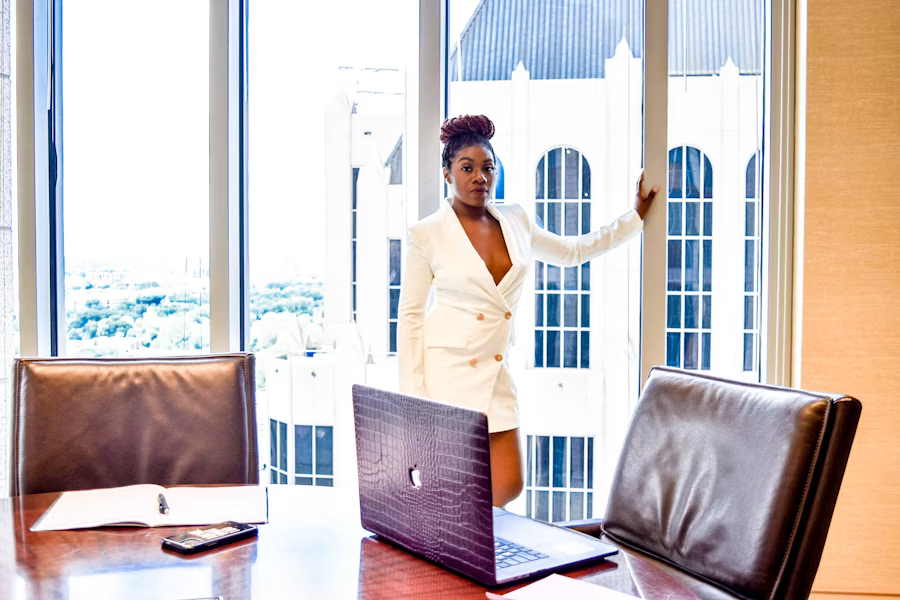 A woman in a white blazer standing near a window in an office