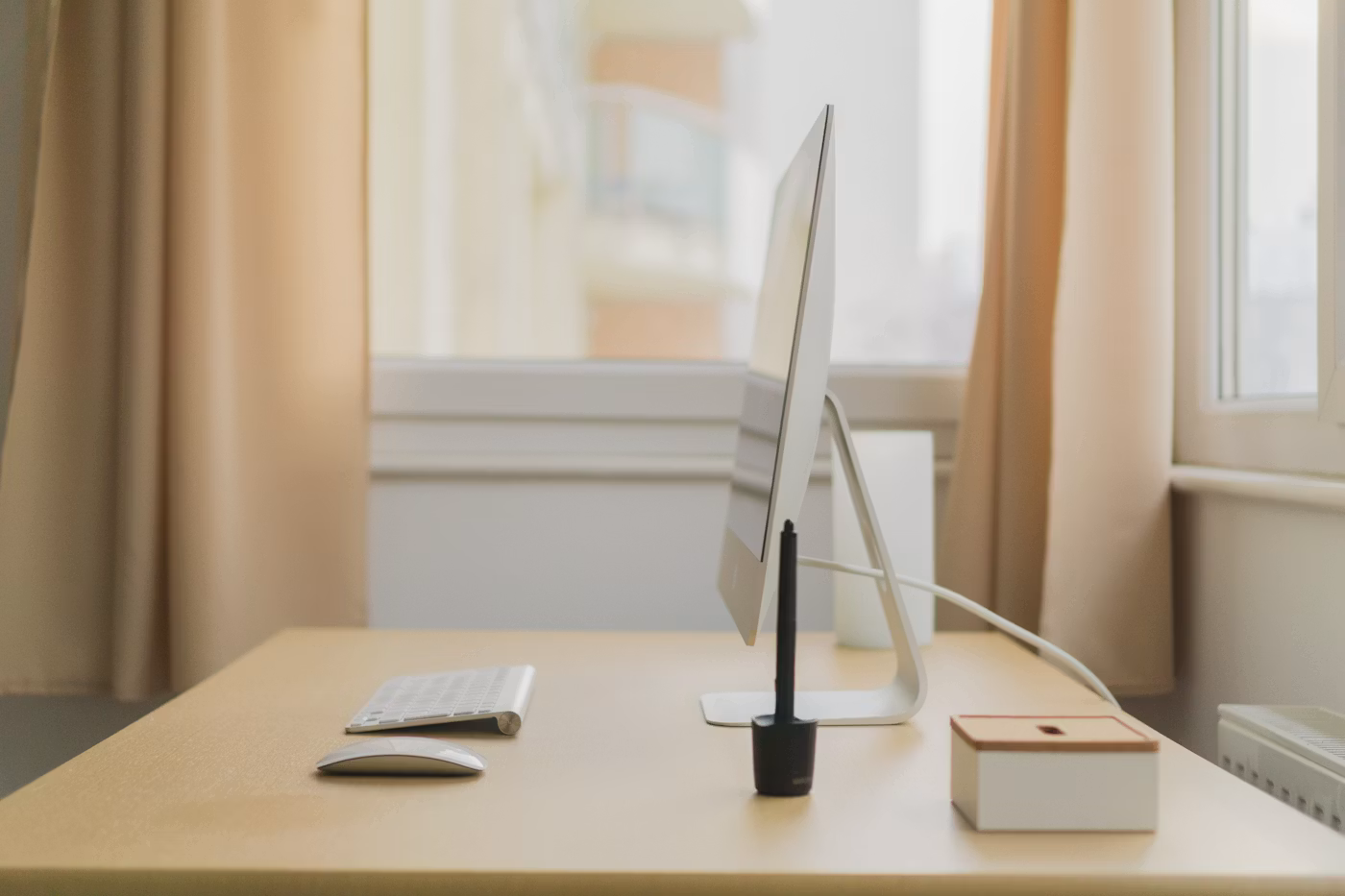 A minimalist desktop computer positioned near a sunlit window in a calm home office