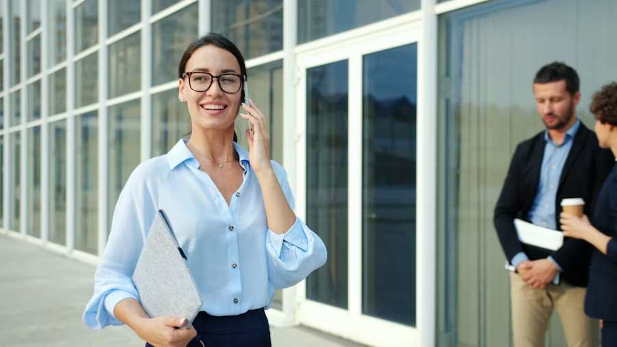 A woman in glasses talking on the phone just outside an office building